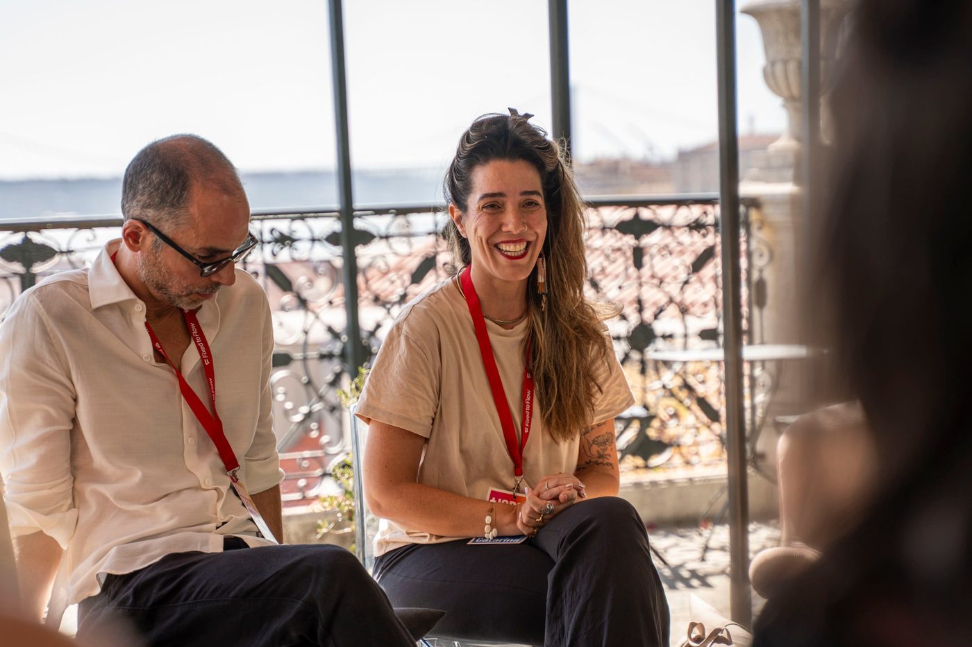 A participant smiling during a conversation on the Lisboa 2036 terrace, with the river and the bridge behind