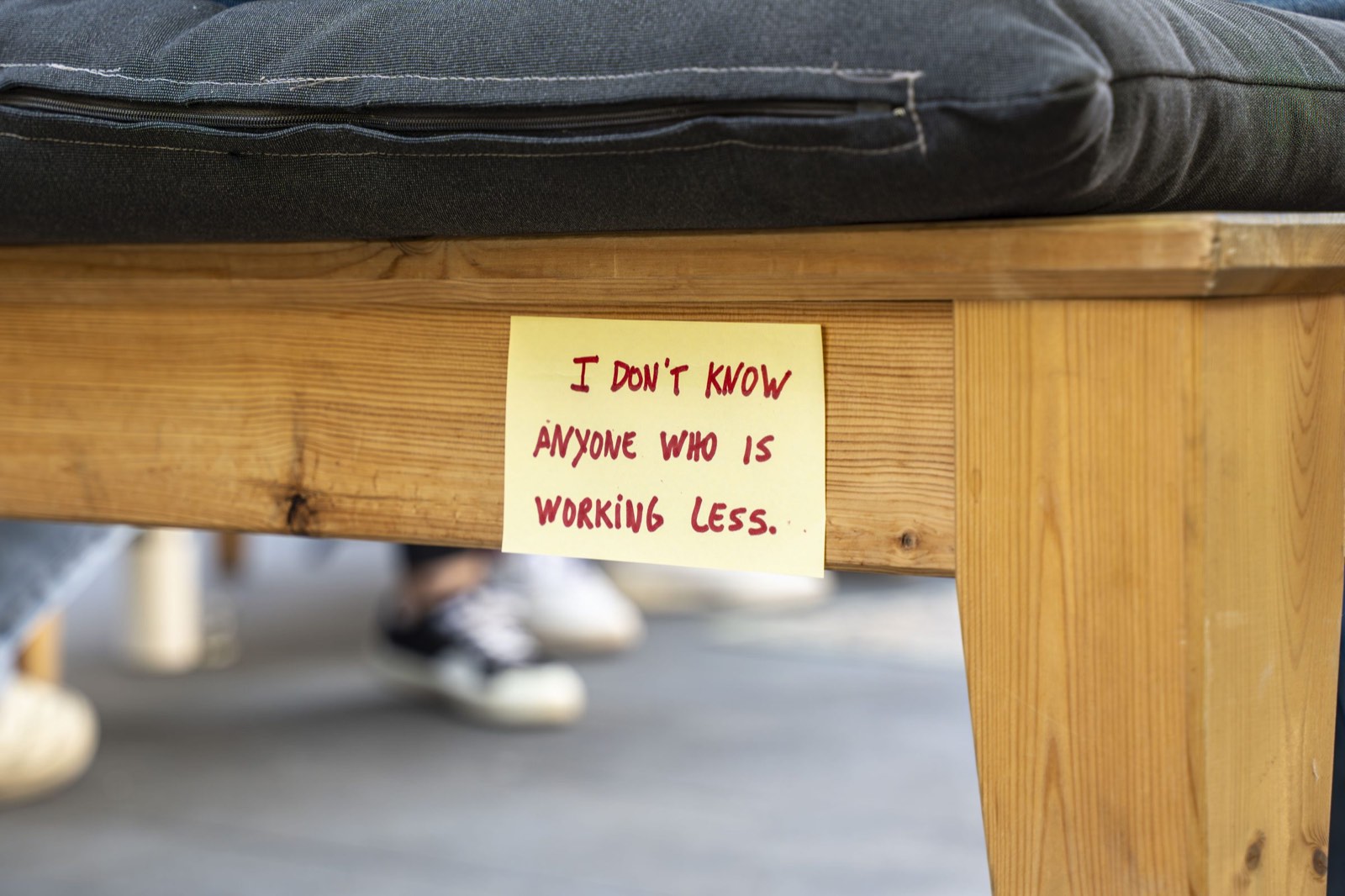 A handwritten sticky note under a bench that reads: I don't know anyone who is working less